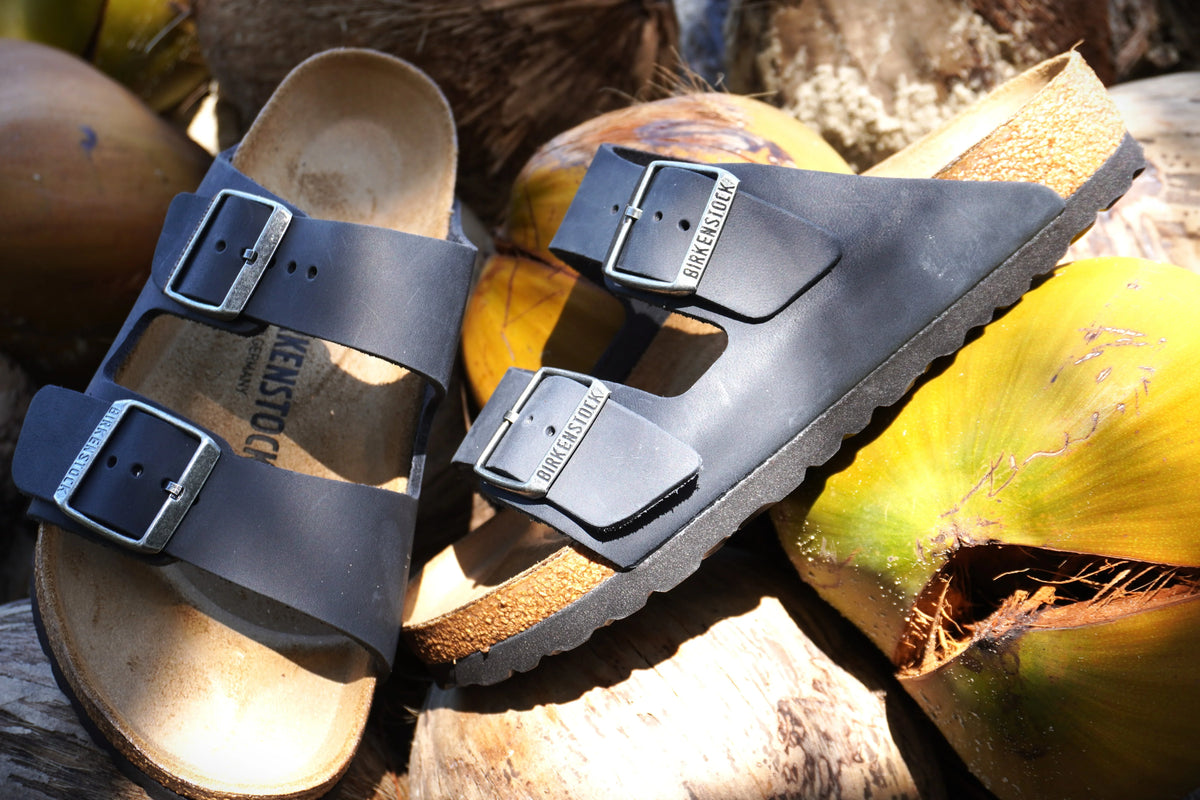 Black Birkenstock sandals with dual buckles on natural wood and coconuts